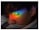 A person with closed eyes is seen with a vibrant rainbow of colors projected onto their face, positioned across the eyelid. The colors range from red, orange, yellow, green, blue, to purple. A tear appears to trail down the cheek, adding a sense of emotion to the scene.