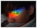 A person with closed eyes is seen with a vibrant rainbow of colors projected onto their face, positioned across the eyelid. The colors range from red, orange, yellow, green, blue, to purple. A tear appears to trail down the cheek, adding a sense of emotion to the scene.