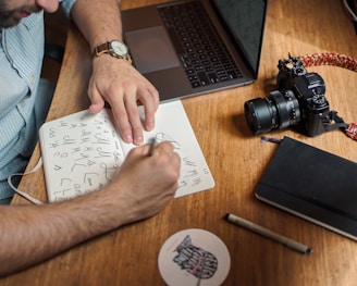 man writing on paper in front of DSLR