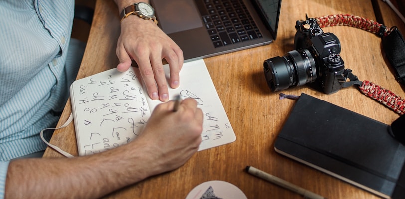 man writing on paper in front of DSLR