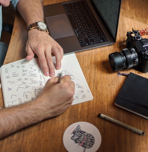 man writing on paper in front of DSLR