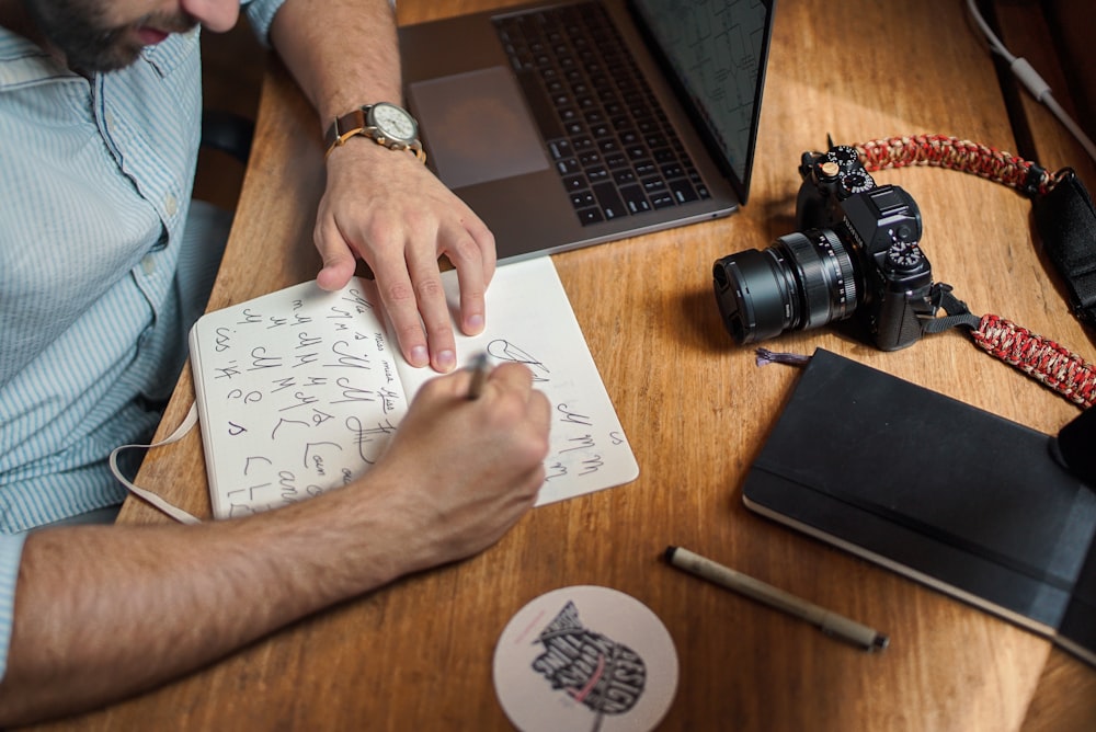 homem escrevendo em papel na frente da DSLR