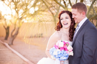 A bride and groom sharing a joyful laugh under a blooming tree during their outdoor wedding.