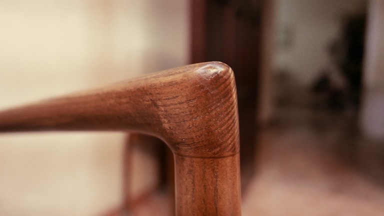 A close-up of a craftsman's hands carefully carving details into a wooden chair armrest.