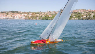 A sleek 3D printed RC sailboat model displayed on a digital blueprint background.