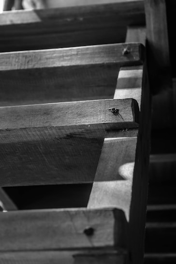 A close-up view of a wooden staircase, showcasing the texture and grain of the wood. The lighting creates shadows that add depth, emphasizing the craftsmanship and detail in the wooden steps and supporting beams.