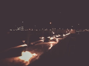 A series of small clay oil lamps are arranged along a parapet in the dark. The soft, warm glow of the flames creates a serene and festive atmosphere against the night sky. A blurred background indicates more lights in the distance, suggesting a celebration or festival.