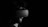 A person is wearing a virtual reality headset in a dimly lit environment. The image is in black and white, emphasizing the contrast between the dark background and the gadget. The person has a beard and short hair, and the headset partially obscures their face.