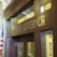 The image depicts the entrance to an office with large wooden doors and a prominent sign that reads 'Office of the Governor' in gold letters. The office is flanked by an American flag and features classical architectural elements, including columns and ornamental details. The atmosphere suggests a formal and official setting.