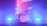 A drum set is illuminated by vibrant colored lights, with shades of pink, purple, and blue creating a dramatic stage effect. The drums, including cymbals, toms, and a bass drum with a visible logo, are positioned centrally, surrounded by a misty, smoky atmosphere that enhances the concert-like setting.