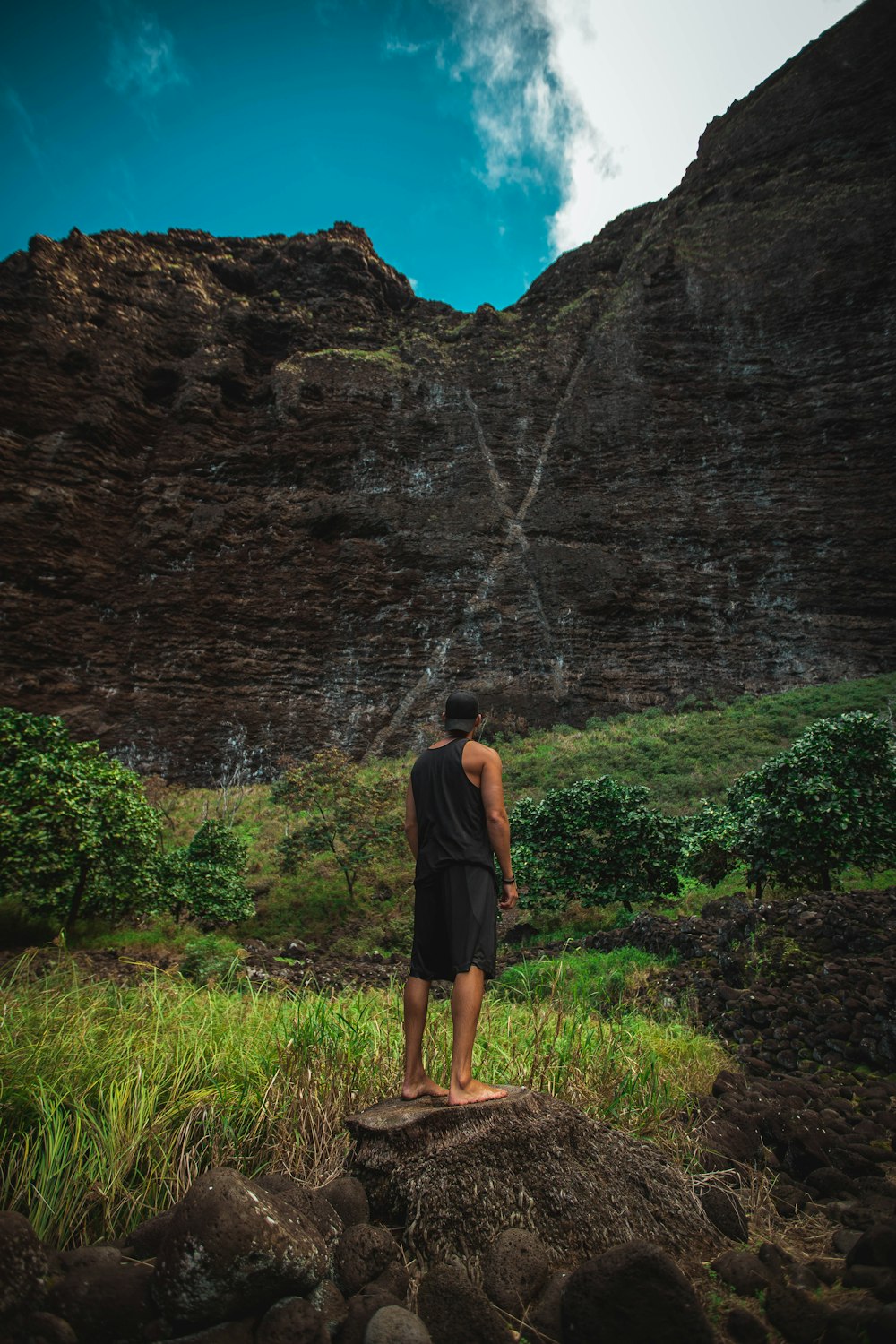 man wearing white black tank top and shorts standing on rock