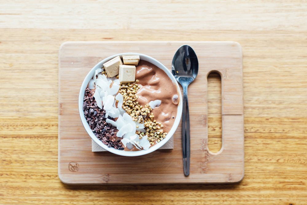 silver spoon and white bowl on brown wooden chopping board