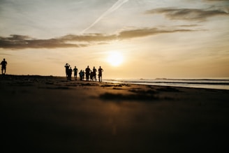 A group of people walking together on a beach at sunset.