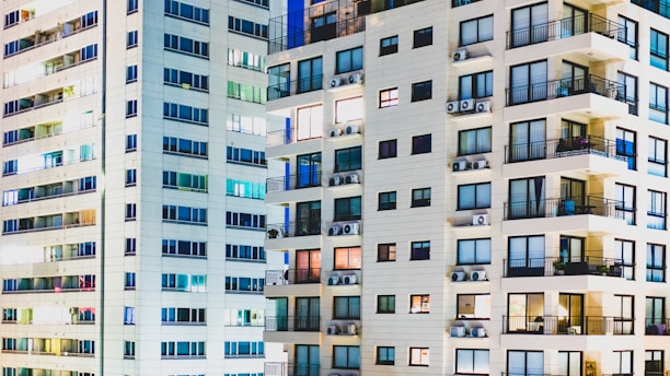 High-rise residential buildings with numerous windows and balconies. Many of the units have visible air conditioning units installed. The structures are predominantly light-colored with large glass windows reflecting light.