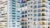 High-rise residential buildings with numerous windows and balconies. Many of the units have visible air conditioning units installed. The structures are predominantly light-colored with large glass windows reflecting light.