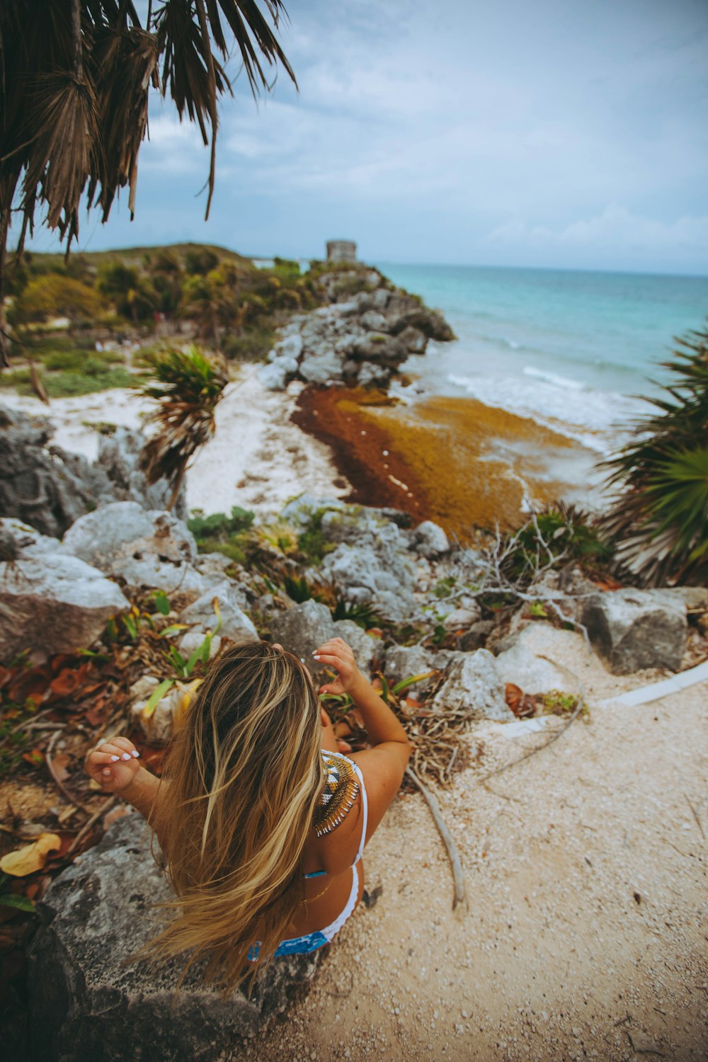 woman sitting on gray rocks near palm trees