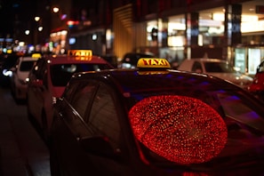 A row of taxis lined up ready for service under bright city lights at night