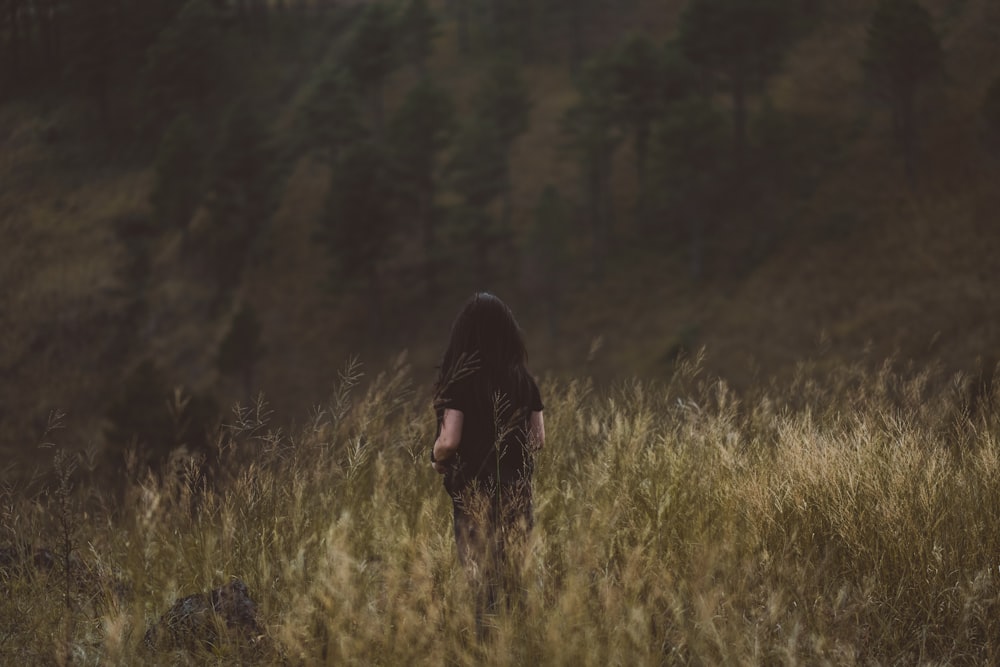 person in black top surrounded by bushes with trees ahead during daytime