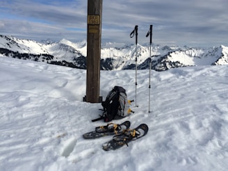 A sherpa handing ski boots to a child near a ski school sign with snowy mountains in the background.
