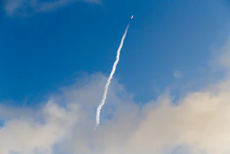 A dynamic video still of a rocket soaring through clouds, leaving a trail.