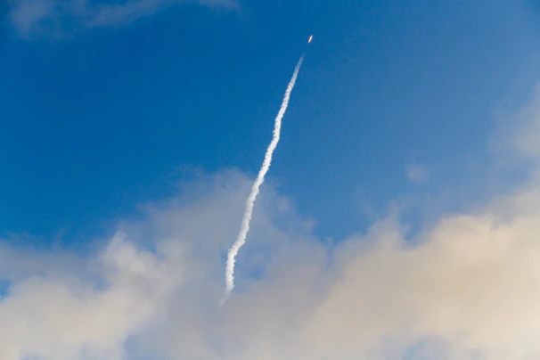 A dynamic video still of a rocket soaring through clouds, leaving a trail.