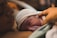 A newborn baby wearing a white knit cap lies on a woman's chest, with a hand gently touching the baby's head. The scene conveys intimacy and warmth.