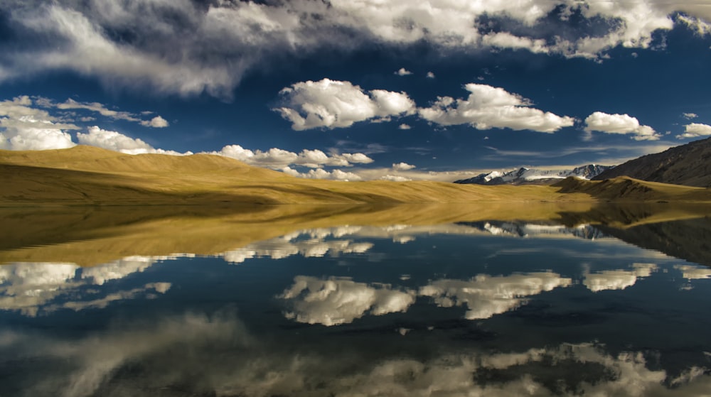 calm body of water near sand under white clouds