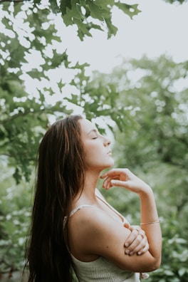 Woman meditating peacefully with glowing skin in a serene outdoor setting.
