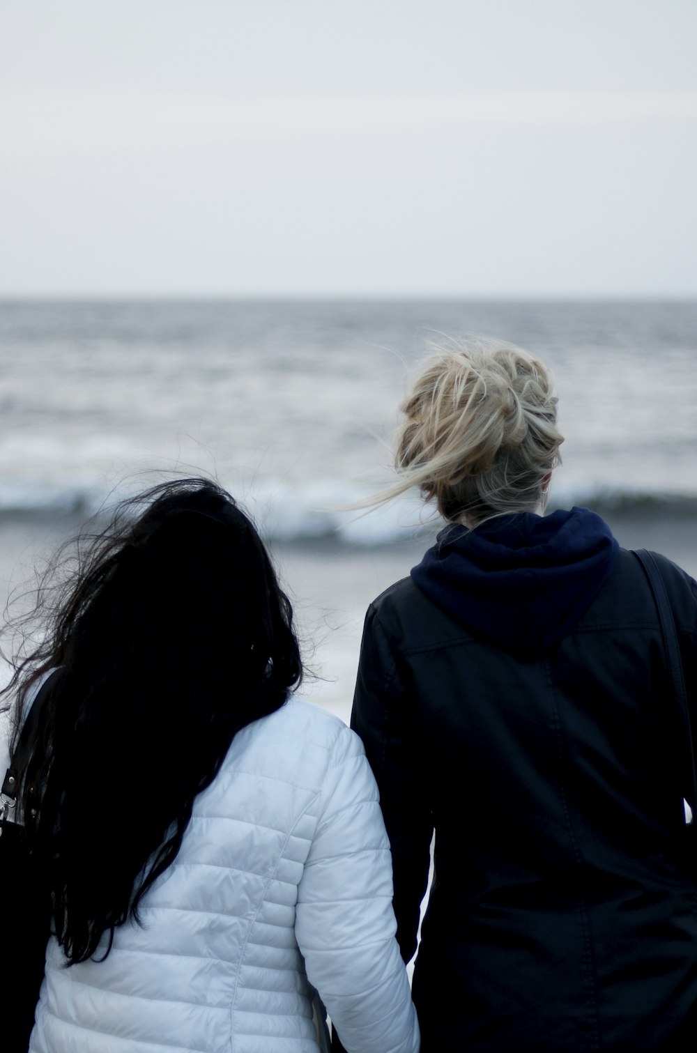 Blonde and brunette stare off into the sea on a cold day