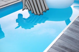 A swimming pool with clear blue water reflects two inflatable pool floats, one shaped like a gray mattress and another resembling an animal with a white body.