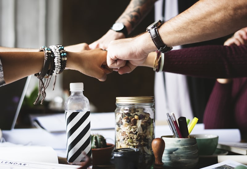 Several people fist bumping over a busy workspace