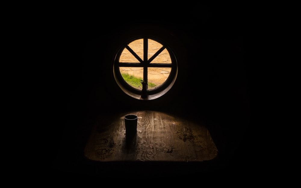 Trinkbecher auf braunem Holztisch in der Nähe des runden Dachbodenfensters