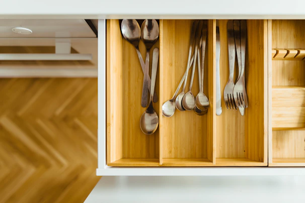 Adjustable drawer dividers separating utensils and kitchen tools in a tidy wooden drawer.