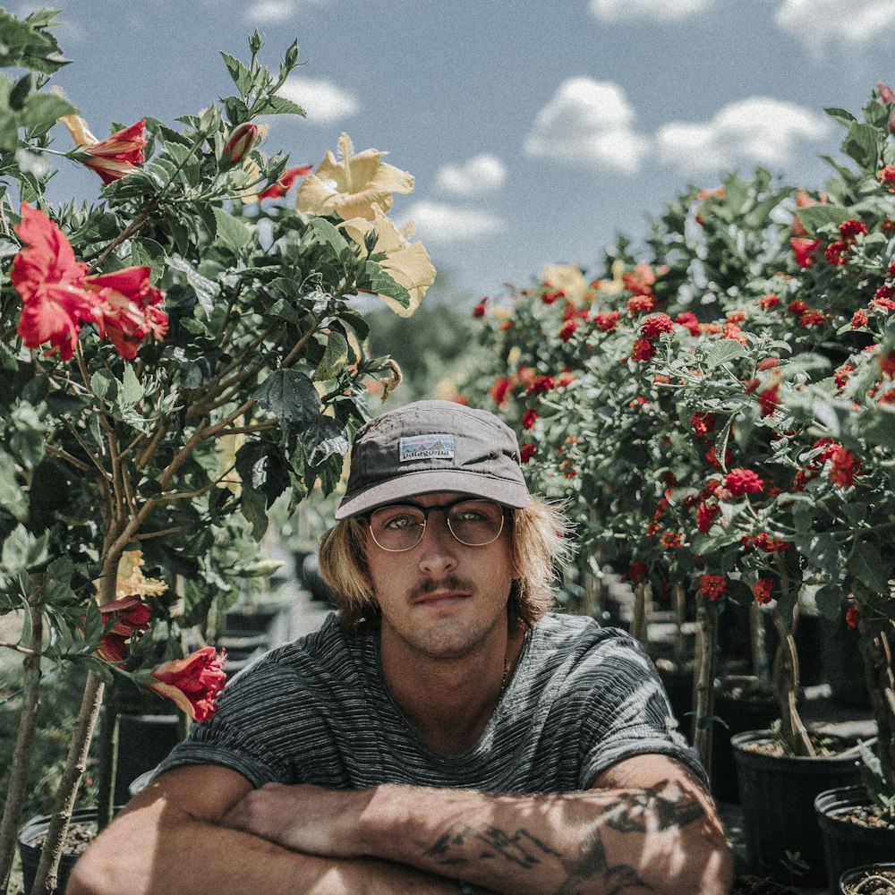 man sitting near hibiscus flowers during daytime