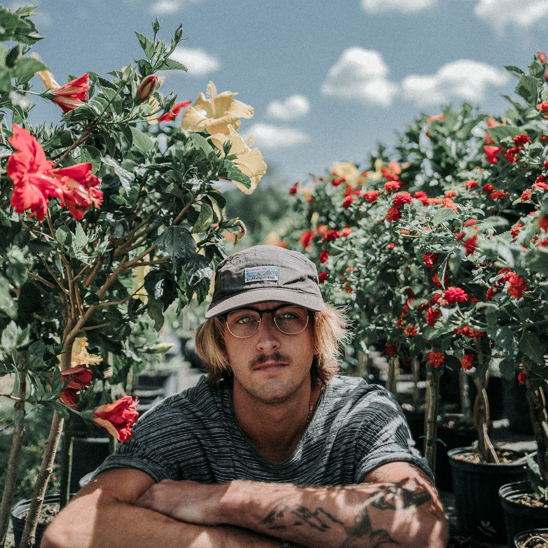 man sitting near hibiscus flowers during daytime