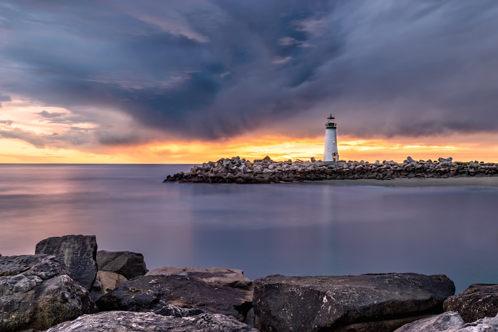 farol branco na costa ao lado do corpo de água