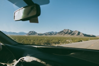 A scenic highway view with a car heading towards distant hills under a clear sky.