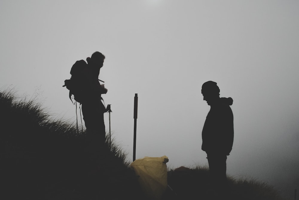Foto da silhueta de dois homens escalando a montanha