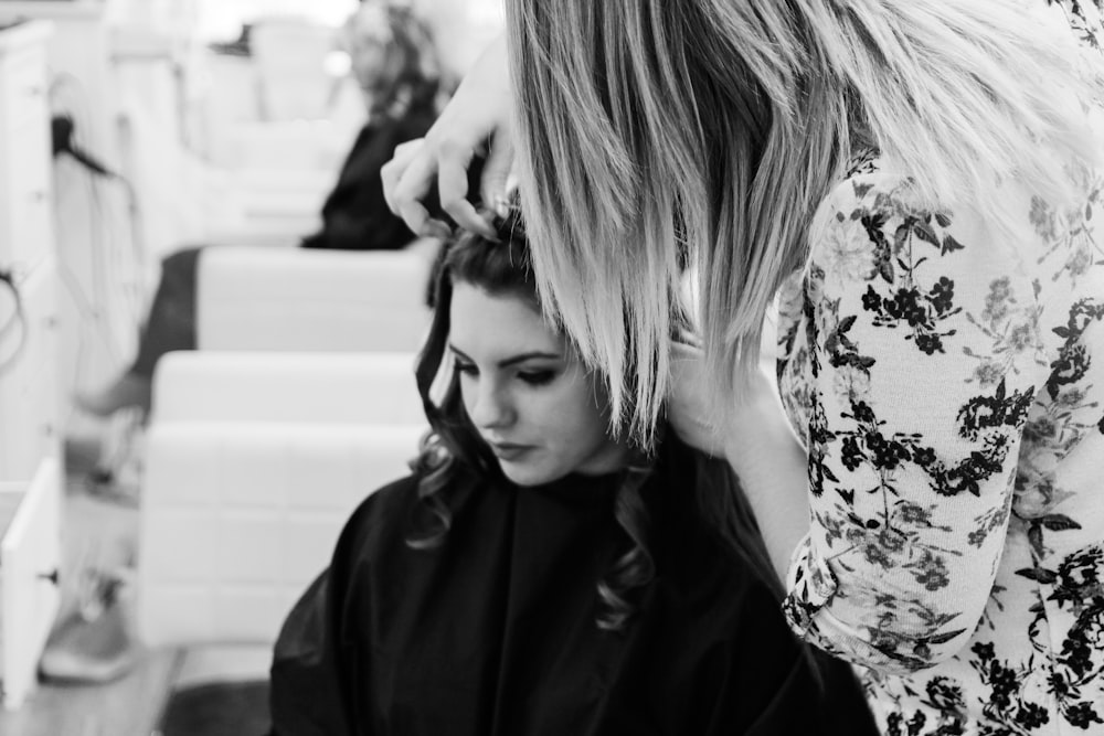 Photographie en niveaux de gris d’une femme se faisant coiffer à l’intérieur d’un salon