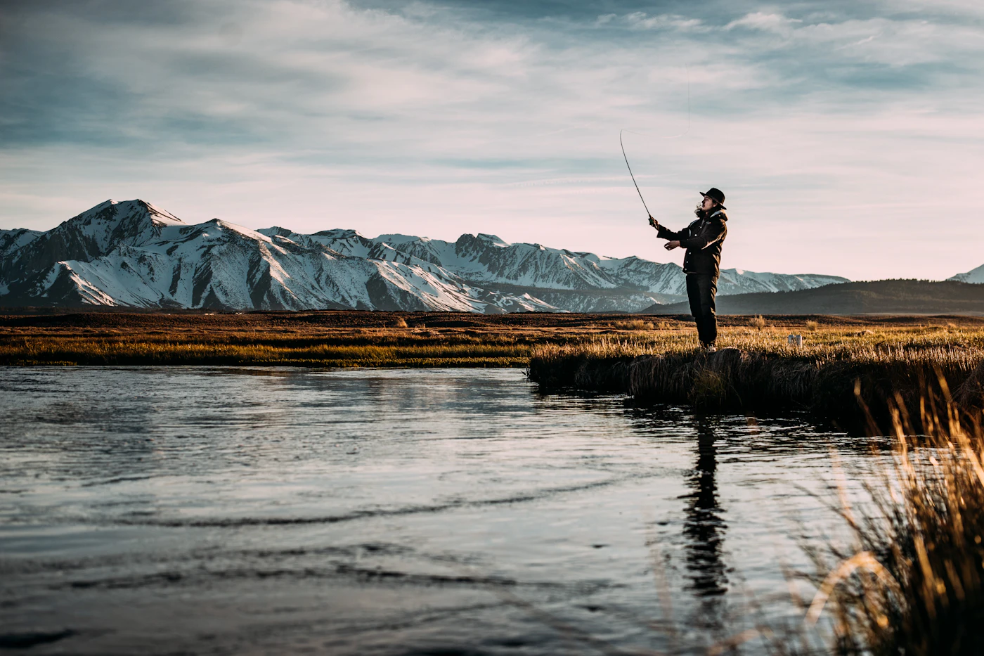 An angler casting a fly line across a clear mountain river at first light