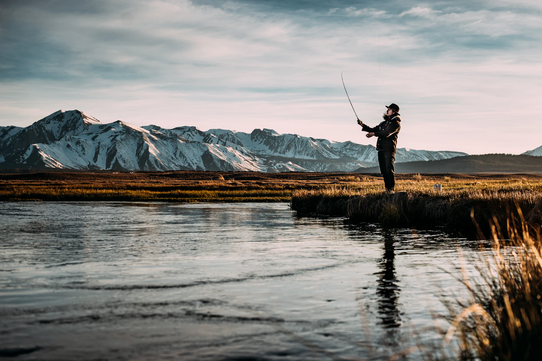 An angler fly fishing in a mountain river at golden hour