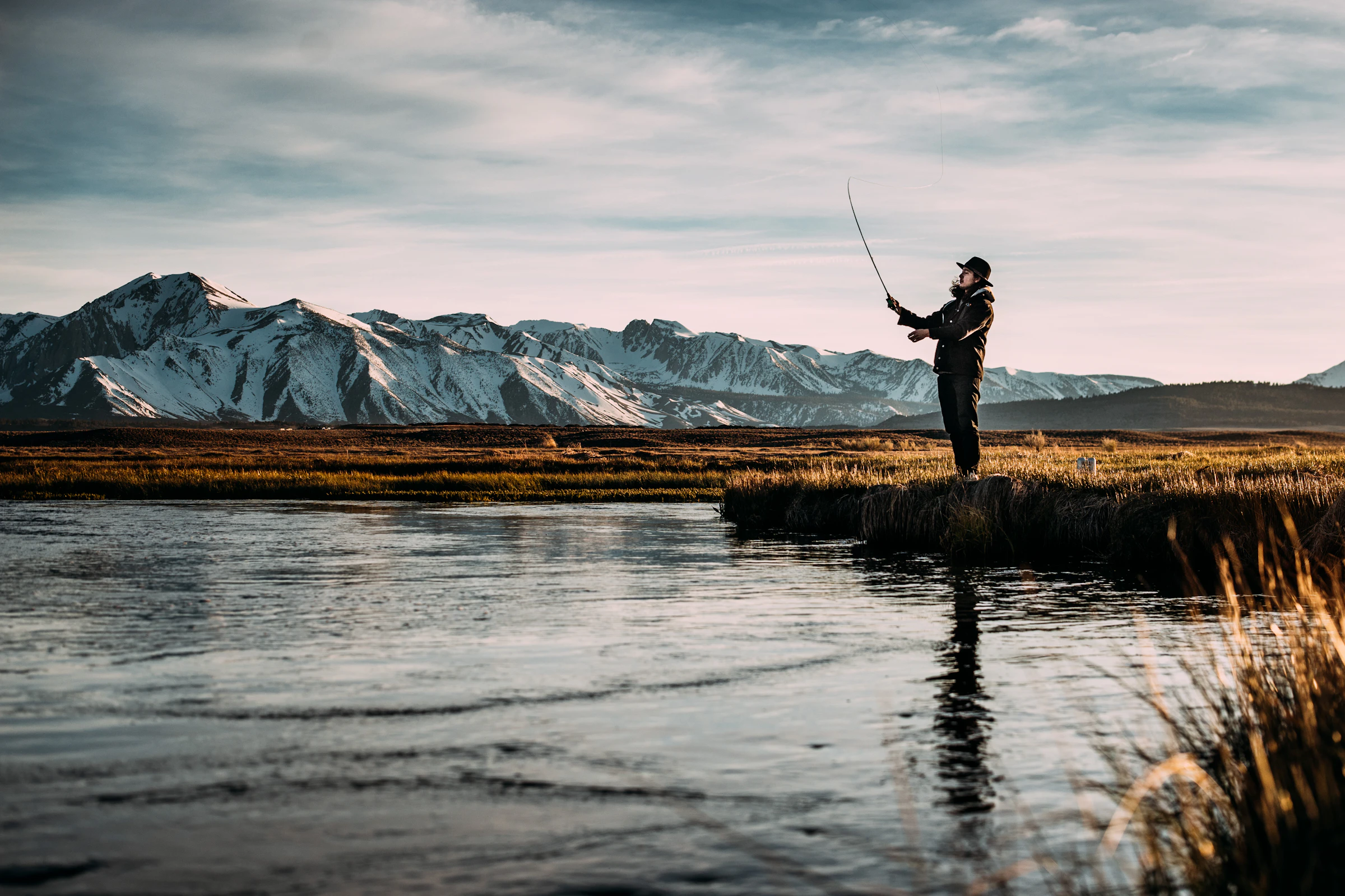 Fly angler casting on a river at the foot of mountains
