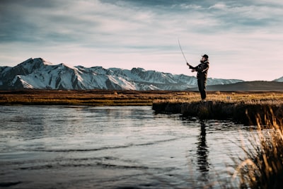 landscape photo of man fishing on river near mountain alps wicked zoom background