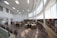 A spacious library with high ceilings, large windows, and numerous bookshelves along the walls. The room is filled with several tables and chairs, arranged neatly, creating a bright and welcoming study environment.