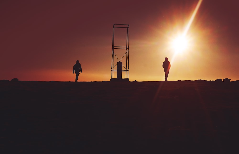 silhouette of two person near gray metal frame during sunet