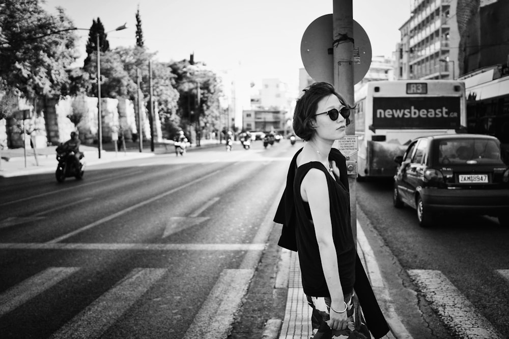 grayscale photo of woman standing beside road signage