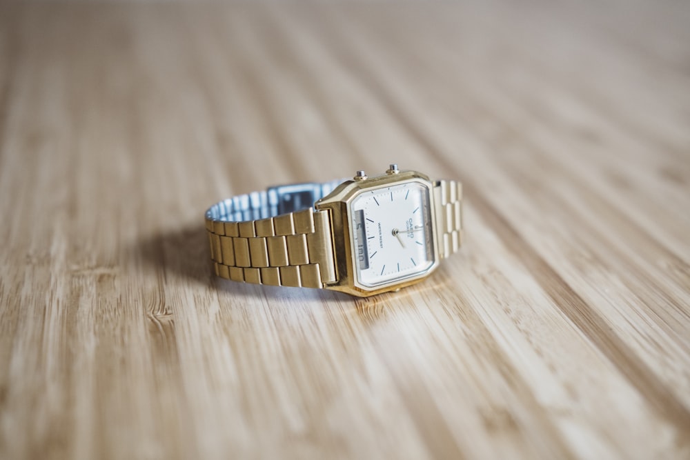 square gold-colored analog watch on brown wooden board