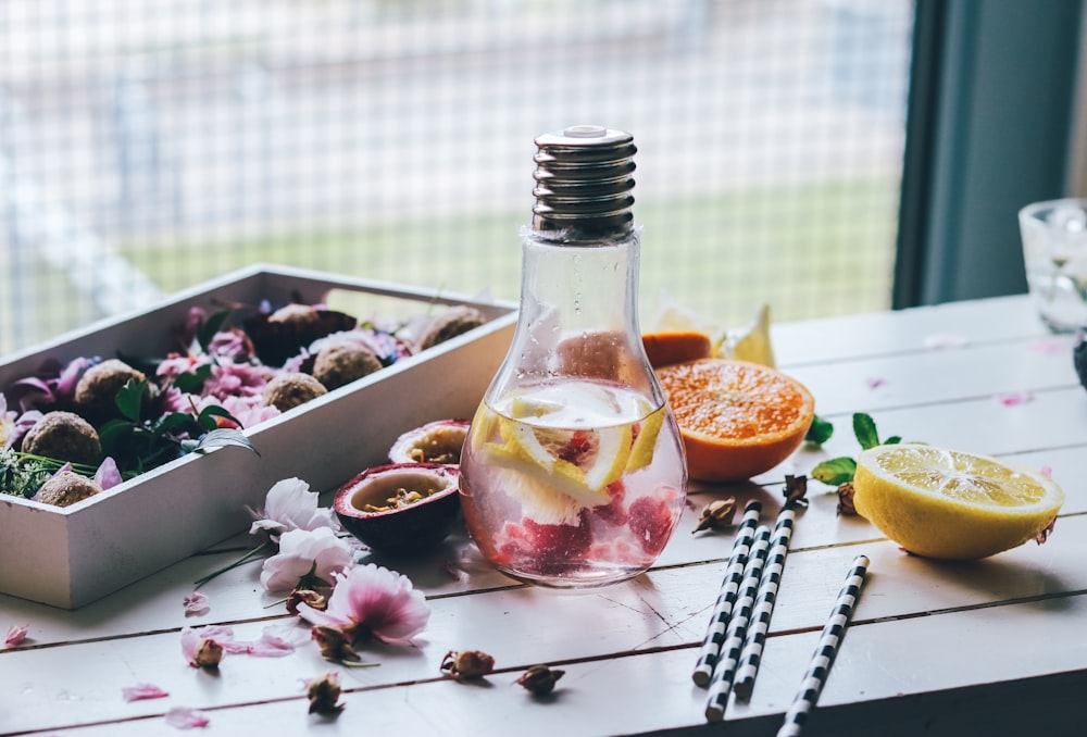 Pichet d’ampoule en verre transparent avec des fruits tranchés de citron et d’orange sur le dessus d’une table blanche