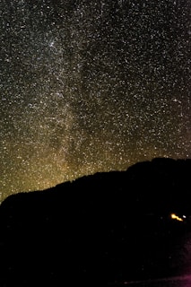 A vast starry sky with a silhouette of a mountain.