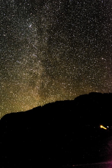 A vast starry sky with a silhouette of a mountain.